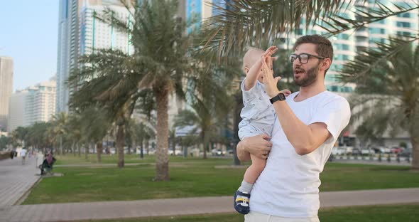 Father Playing with Sons in the Summer Around Palm Trees and Buildings