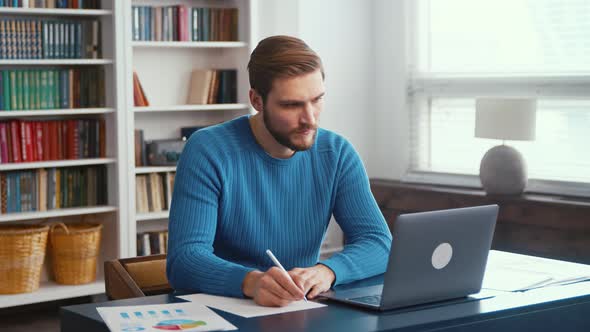 Young teacher taking notes in notebook using laptop