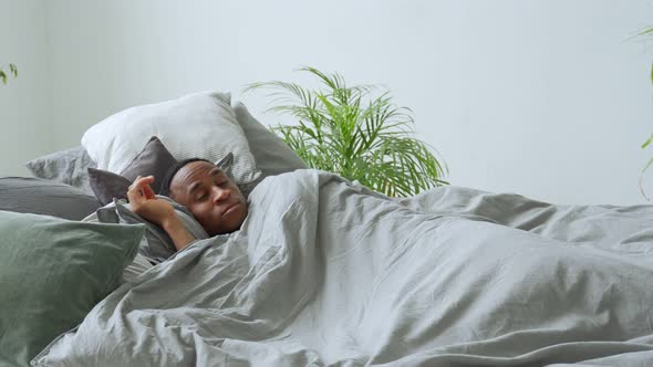 Young Black Man Person Waking Up at Bedroom. Happy African Guy Stretching in Bed in Morning. Young