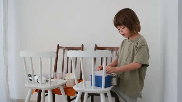 Little Boy Kid Plays with Food Products on Chairs in Room