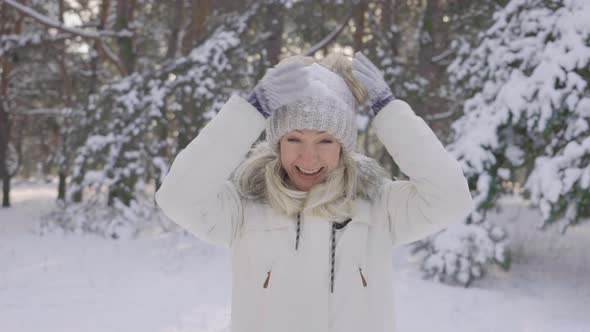 Happy Pretty Girl in Warm Winter Clothes is Blowing Snow From Her Hat and Laughing Happily