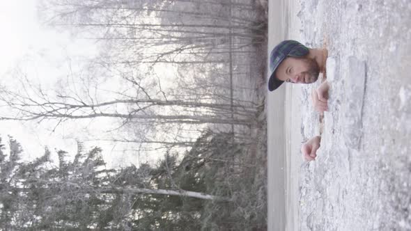 VERTICAL - A rugged bearded ice bather sits in his ice hole in a Swedish lake