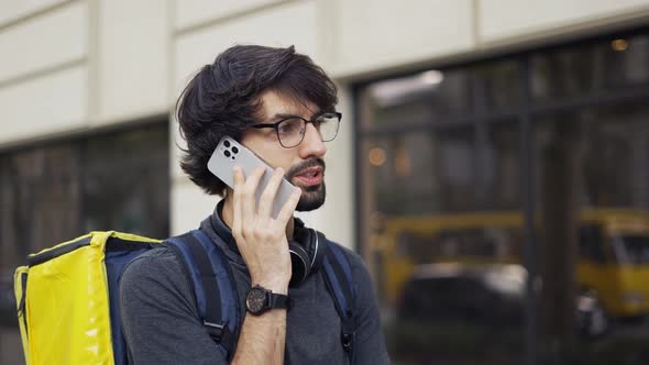 Delivery Man with Yellow Backpack Calling to a Client on the Street