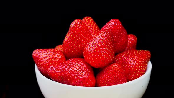 Strawberries without tails lie in white bowl or plate. It rotates