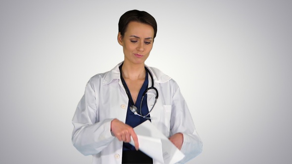 Beautiful young doctor throwing paper on gradient background.