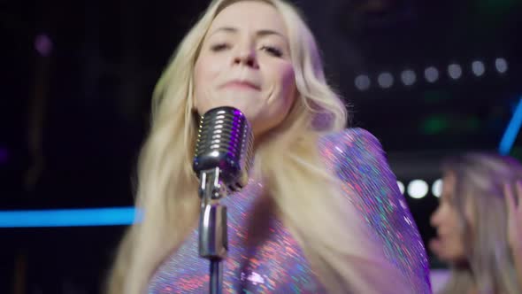 Confident Talented Woman Singing Song with Microphone Smiling As Blurred Crowd Dancing at Background