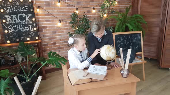 Schoolchildren - a boy and a girl are studying the globe with a magnifying glass