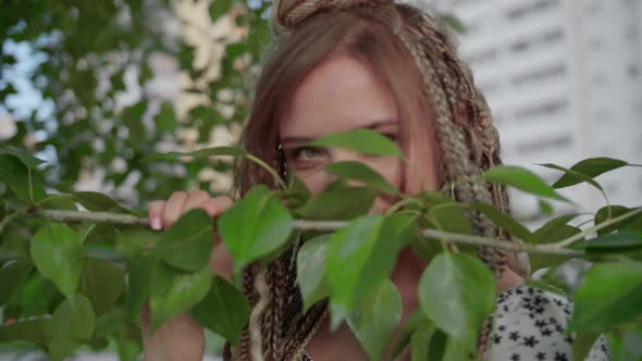 A Cute Girl with Dreadlocks Poses By a Tree with Leaves