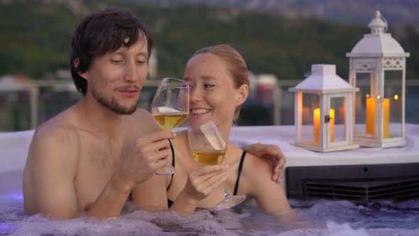 A Young Man and Woman are Relaxing in the Hot Tub on a Rooftop with a View on Mountains During