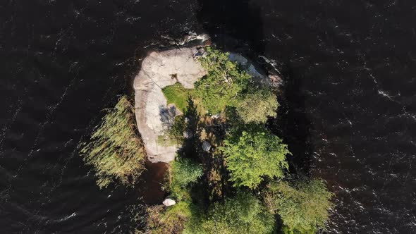 Aerial View of a Small Rocky Island with Green Trees and Grass in the Middle of a Large Lake with