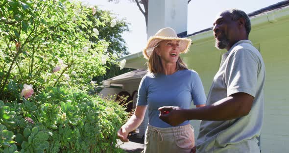 Diverse senior couple in their garden looking at plants and talking in the sun