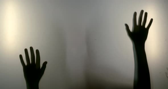 Close-up Shadows of a Woman's Hands and Silhouette Reflected Behind the Glass