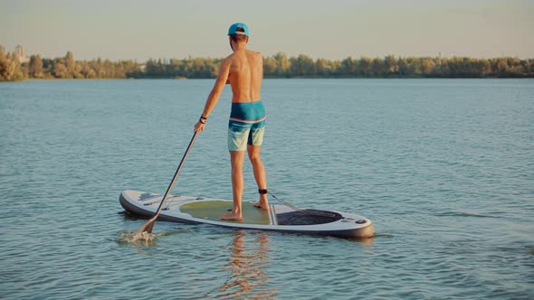 Man Floating On Sup Board At Idyllic Evening. Swimming On Stand Up Paddle Board. Surfer Water Sport