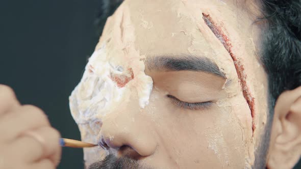 Make up artist coloring prosthetic insert on man's face and making Halloween mask