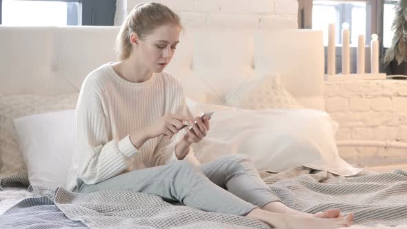 Online Shopping via Smartphone by Young Woman Sitting in Bed