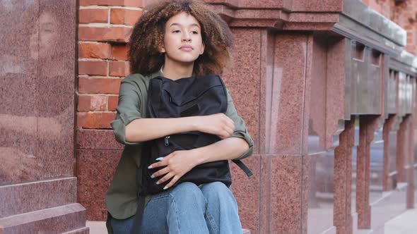 Pensive Ethnic Black Girl with Curly Afro Hair Sitting on Stairs Outdoors Resting Her Head on Travel