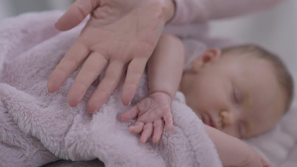 Little Infant Hand and Adult Female Palm with Cute Blurred Baby Girl Sleeping at Background