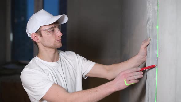 The master applies laser level marking the wall in a house under construction