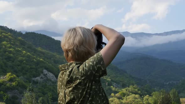 Blond Woman Photographer Photographs Alpine Green Landscape During Sunset with a Professional Camera