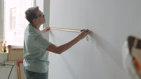Woman Measuring Wall with Tape in Home under Renovation