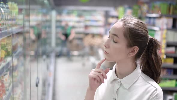 A Girl Shopper Looks at the Refrigerator with Food in the Supermarket