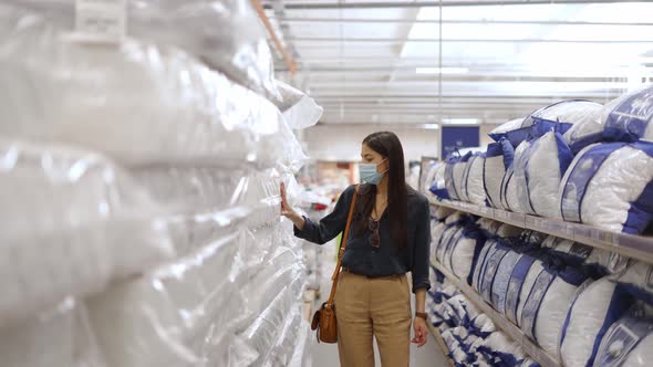 Woman Wearing Face Protective Mask Looking at Quality of Different Mattresses and Pillows for Bed