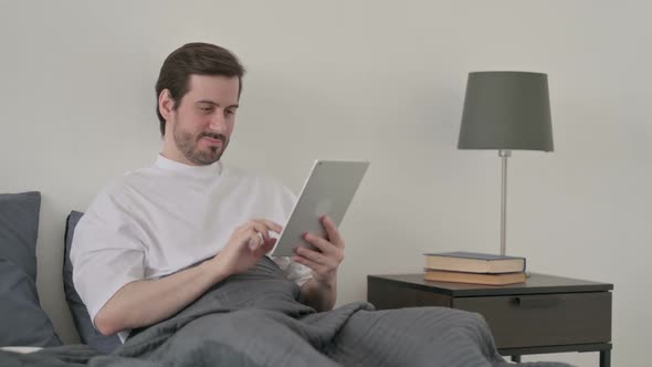 Young Man Using Tablet While Sitting in Bed