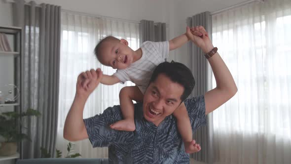 Happy Little Son Sitting On The Parent's Shoulders Walking At Home