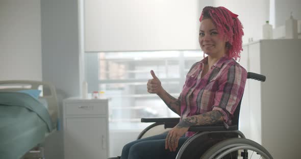 Young Woman with Pink Hair Sit in Wheelchair and Shows Thumbs Up