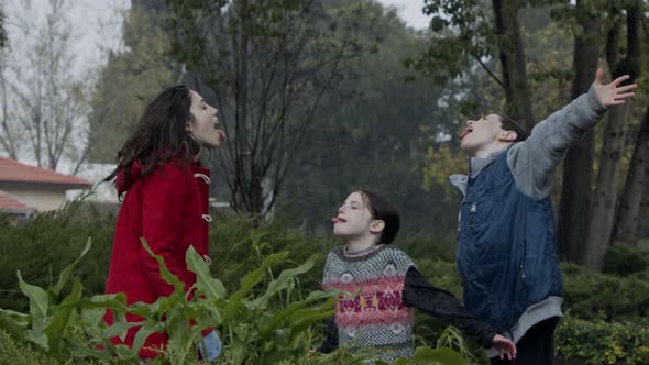 Three kids standing enjoying the pouring rain in slow motion