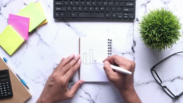 Man Drawing Bar Chart on Notepad Top Down 