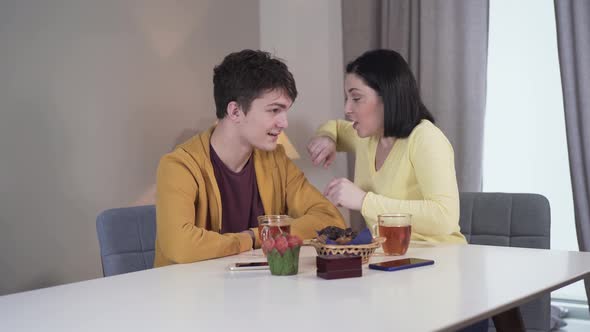 Middle Shot of Joyful Young Caucasian Woman Telling Jokes To Teenage Boy As Sitting at the Table