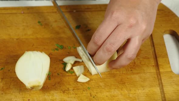 A close-up of the cook taking a peeled onion from his plate. He puts it on the kitchen board