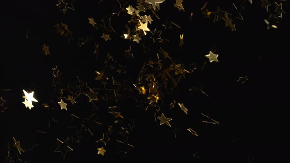 Star shpe gold confetti fly after being exploded against black background. 4K 30fps. Slow Motion.