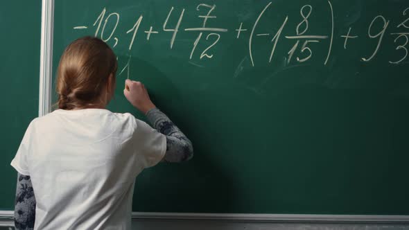 Back View of School Girl Doing Math Task on Blackboard in Class