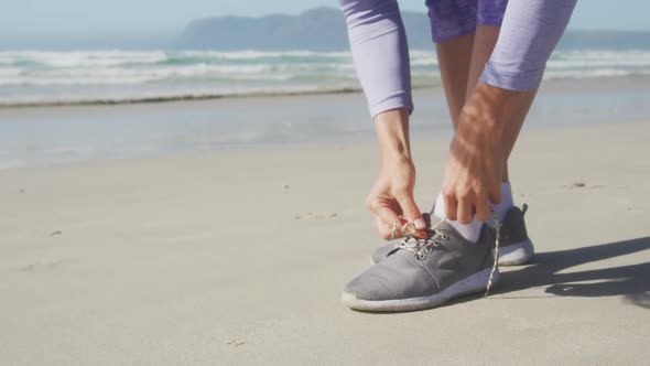 Athletic woman lacing up her shoes on the beach