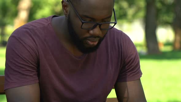 Afro-American Man Sitting on Bench and Searching for Work on His Smartphone