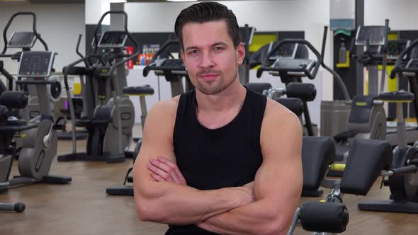 A Young Fit Man Folds His Arms Across His Chest and Smiles at the Camera in a Gym - Closeup