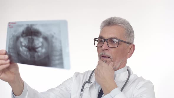 White Middleaged Doctor Man Looks Carefully at the Xray and Thoughtfully Studies Image Touching His