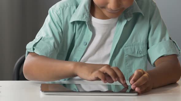 Biracial Boy Sitting at Table with Tablet Scrolling Screen Modern Technologies