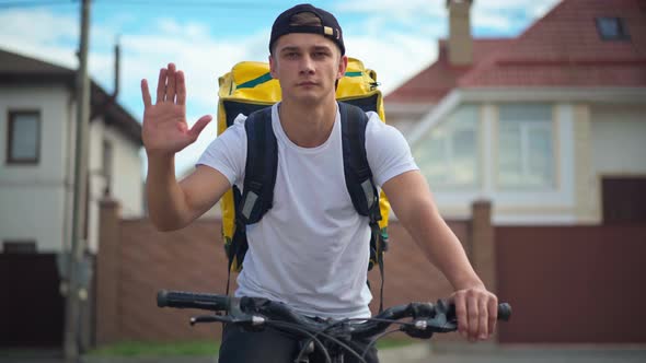 Medium Shot Portrait of Young Delivery Man Raising Palm Asking for Giving Way Leaving on Bike