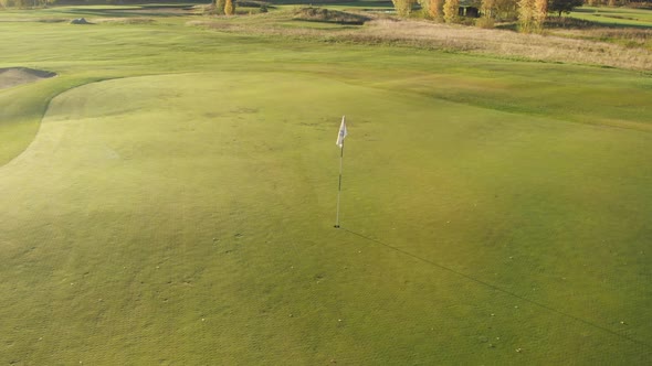 Moving along a green beautiful golf course with a white flag next to a sand bunker.