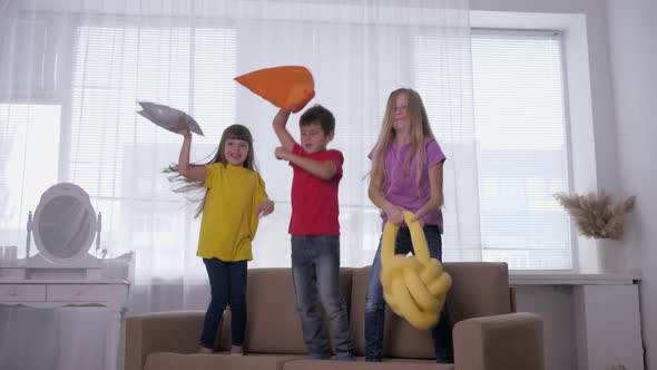 Active Children Have Fun and Jumping on the Couch with Pillows in Hands Against the Background of