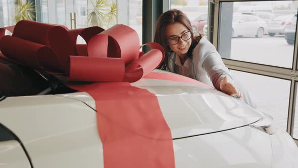 Happy Woman Hugging Her White New Car with Red Bow on Hood