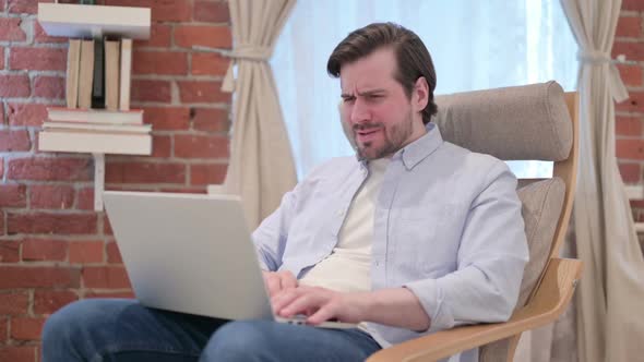 Casual Young Man with Laptop Reacting to Loss on Sofa