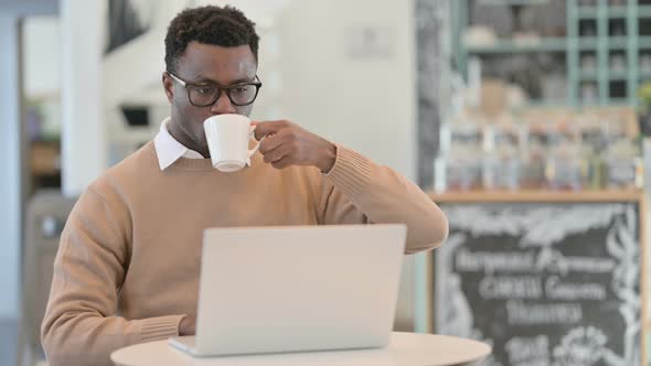 Creative African Man Drinking Coffee While Using Laptop in Cafe