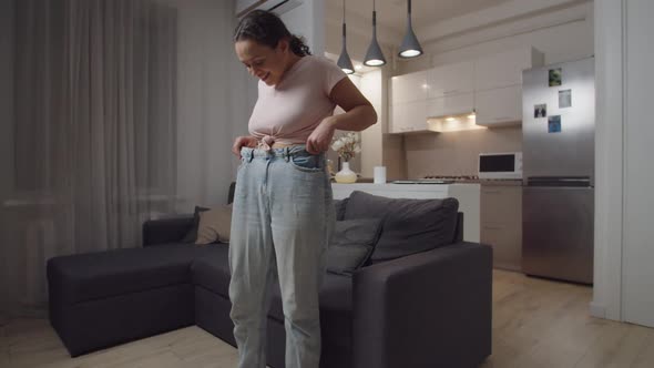 Woman Wearing Loose Jeans Admiring Body After Weight Loss Indoors