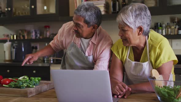 Senior mixed race couple using laptop preparing food in kitchen