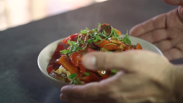 The cook puts on the table a plate of steaming food with pasta and vegetables