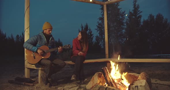The Couple Sings Songs with a Guitar Around the Fire